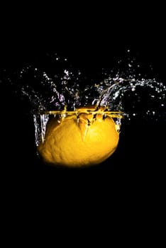 A lemon dropped into water creating a splash and bubbles. Isolated on black.