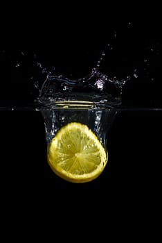 A lemon dropped into water creating a splash and bubbles. Isolated on black.