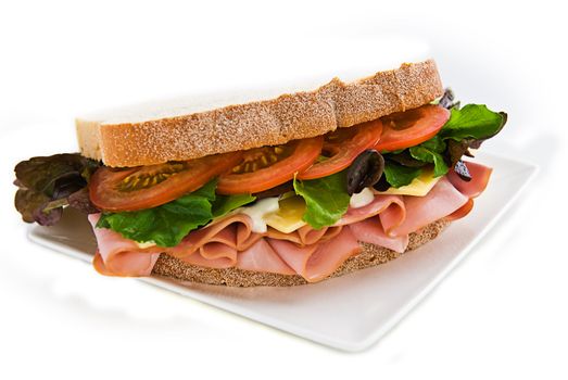 A gourmet sandwich of ham, cheese, lettuce, tomato and mayonaise isolated on white.