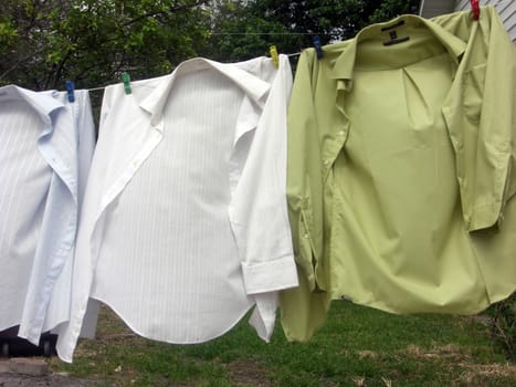 A few man's shirts are hanging on a clothes line to dry.