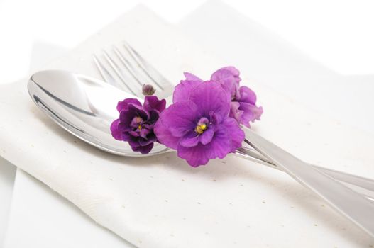A spoon with a fork on a napkin and a plate decorated with violets