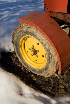 Fragment of old yellow tractor wheel covered with mud.