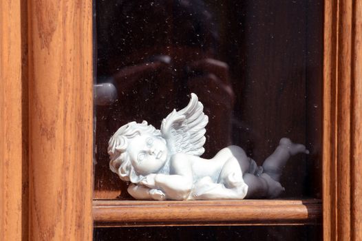 White ceramic angel on the wooden window sill behind the glass.