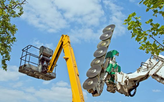 chainsaw for cutting branches and cherry-picker on blue sky background