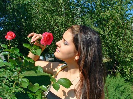 Young girl enjoys charming aroma of a rose in bright, a sunny day.