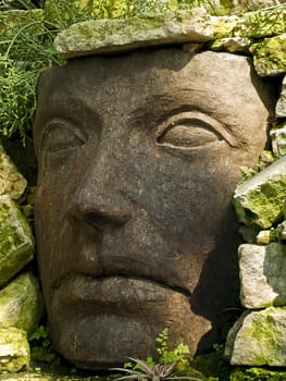 Stone face carving in a summer garden.