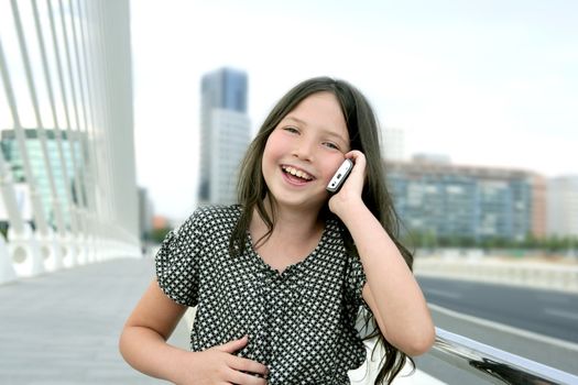 Adorable teenager little girl talking phone downtown in city bridge