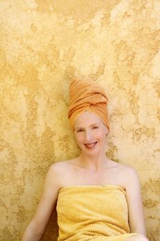 Beautiful woman with orange towel in head over yellow golden wall