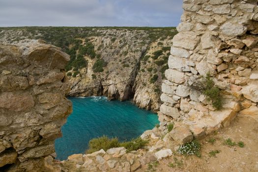 A hole in an old fort wall, overlooking an aqua-marine body of water in the Algarve, near Sagres, Portugal.