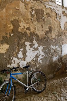 An old bike up against an old textured wall.