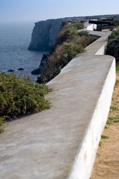 Along the fort walls, focus on a cannon midway, with steep cliffs in the distance.  Fortaleza de Sagres, Sagres, Portugal