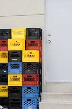 Multiple colored stacked crates beside the back door of a retail building.