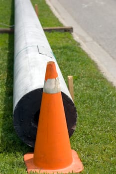 A new hydro pole waiting to be installed, stored by the side of the road on the grass.