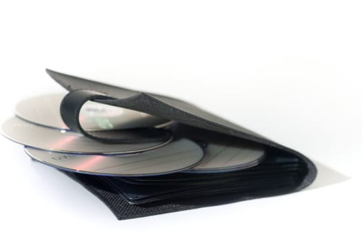 A black leather CD/DVD wallet with scattered DVD media, isolated on white.