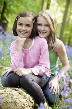 Two girls sitting together in a wood full of bluebells