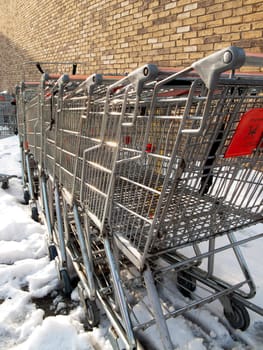 A bunch of old shopping carts, with a brick wall in the background, surrounded by snow.