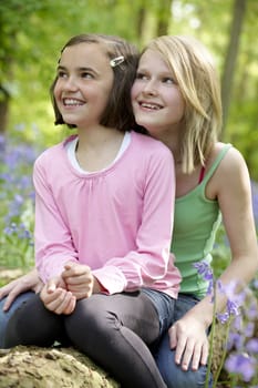 Two girls sitting together in a wood full of bluebells