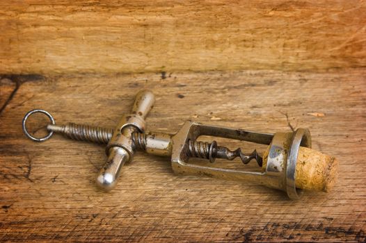 old corkscrew with a cork on the background of wooden boards