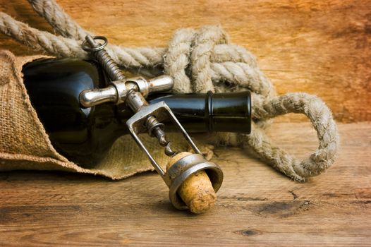 old corkscrew with a cork and a bottle on the background of wooden boards