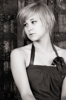 Beautiful blond sitting against an antique trunk with a serious expression