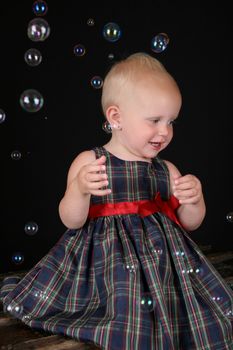 Cute blond toddler girl surrounded by bubbles sitting on a wooden trunk
