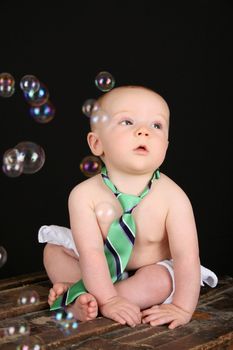 Cute baby boy sitting on an antique trunk looking at bubbles