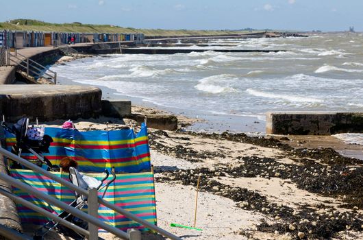 Tourists shelter from wind on cold day on English beach in Kent
