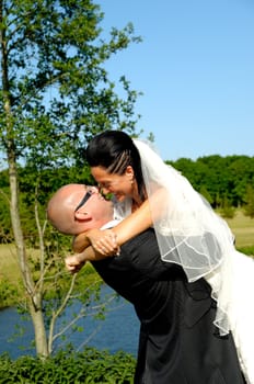 Groom is lifting his bride up in a park.