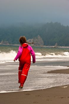 young girl in red rain clothes skipping down beach