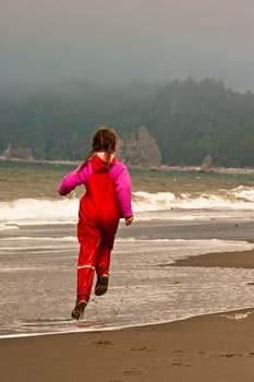 young girl in red rain clothes, skipping down beach shore