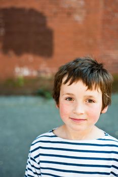young boy in blue white stripes shirt on city street with brick wall behind