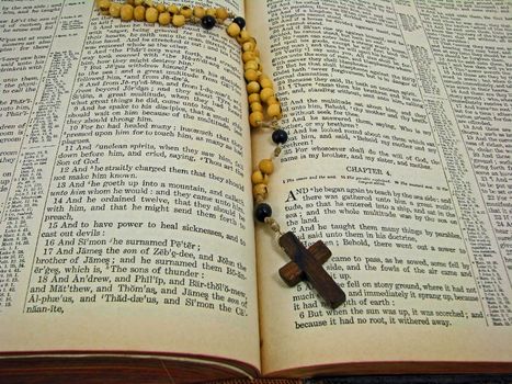 A rosary laying on a worn antique Bible.
