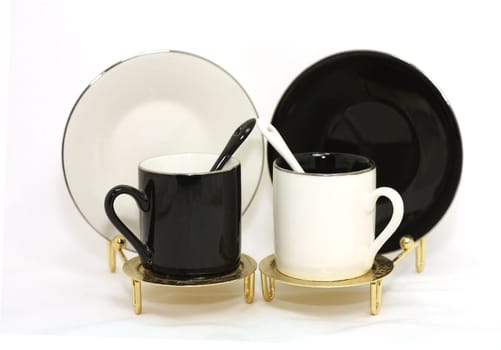 Black and white cups, saucers, spoons on gold stands.
