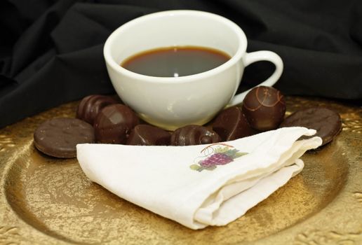 Cup of coffee with chocolate candy on a gold platter.
