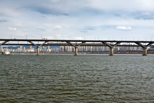 Bridge over Han river in Seoul wtih subway train and cars with apartments on background