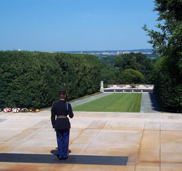 A soldier stands a attention at the Tomb of the Unknowns in Arlington National Cemetery, Washington, DC, USA. Guards are on duty 24 hours a day 365 days a year. The tomb contains the remains of unknown American soldiers from World War I, World War II and the Korean Conflict. The skyline of Washington, DC, USA can be seen in the distance.