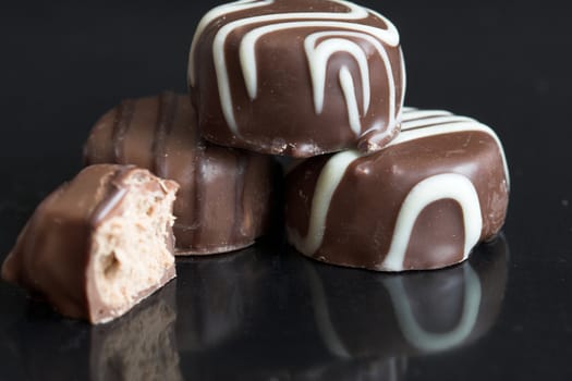 Some delicious chocolates lying together on a black background with reflection