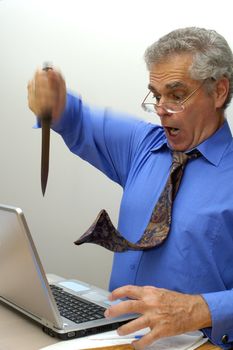 An older businessman fed up with his laptop, stabs it with a knife.