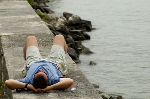 A lone man lies beside a lake, relaxing, with an empty wineglass beside him. Space for text on water.