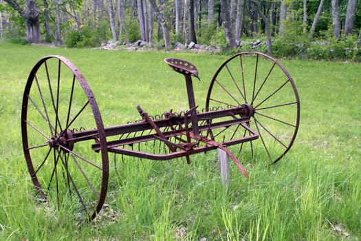 an obsolete antique hay rake sits in a green field