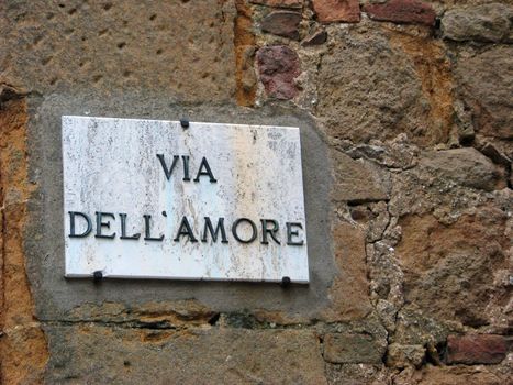 The street sign for Via Dell' Amore in the historic renaissance city of Pienza, Italy invites couples on a romantic stroll along the street of love.