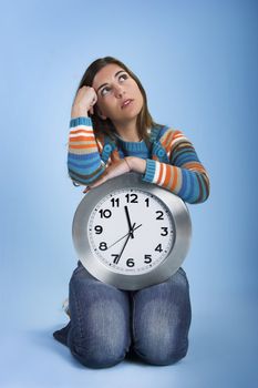 Beautiful women over knees holding a big clock with a blue background