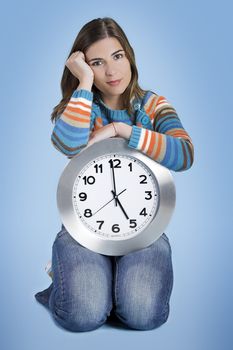 Beautiful women over knees holding a big clock in a blue background
