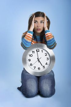 Beautiful women over knees holding a big clock in a blue background