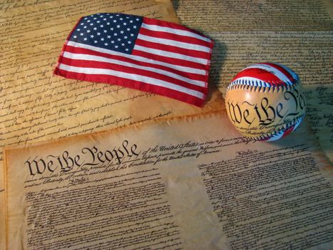 A copy of the Constitution of the United States accompanied by a flag and a baseball with the words of the Constitution on it.