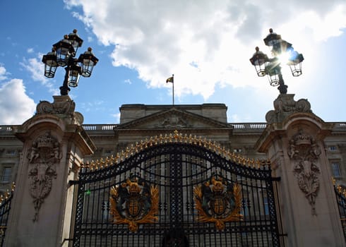 The gates of Buckingham Palace in London, England with the sun shining through the lampost.
