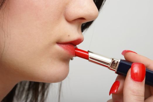 A young girl is putting on red lipstick.