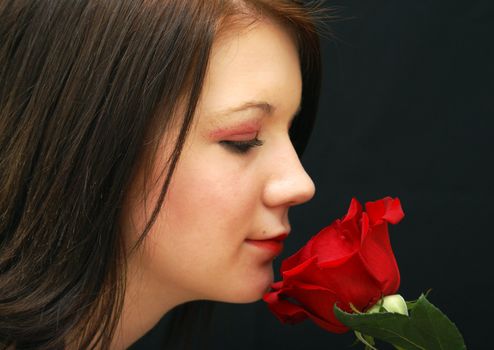 A girl holds a red rose close to her face to smell it.