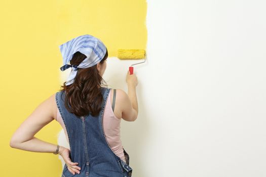 Photo of a female painting a wall with a roller and yellow paint.