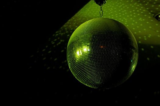 Disco ball in motion reflecting green light in night club with copy-space